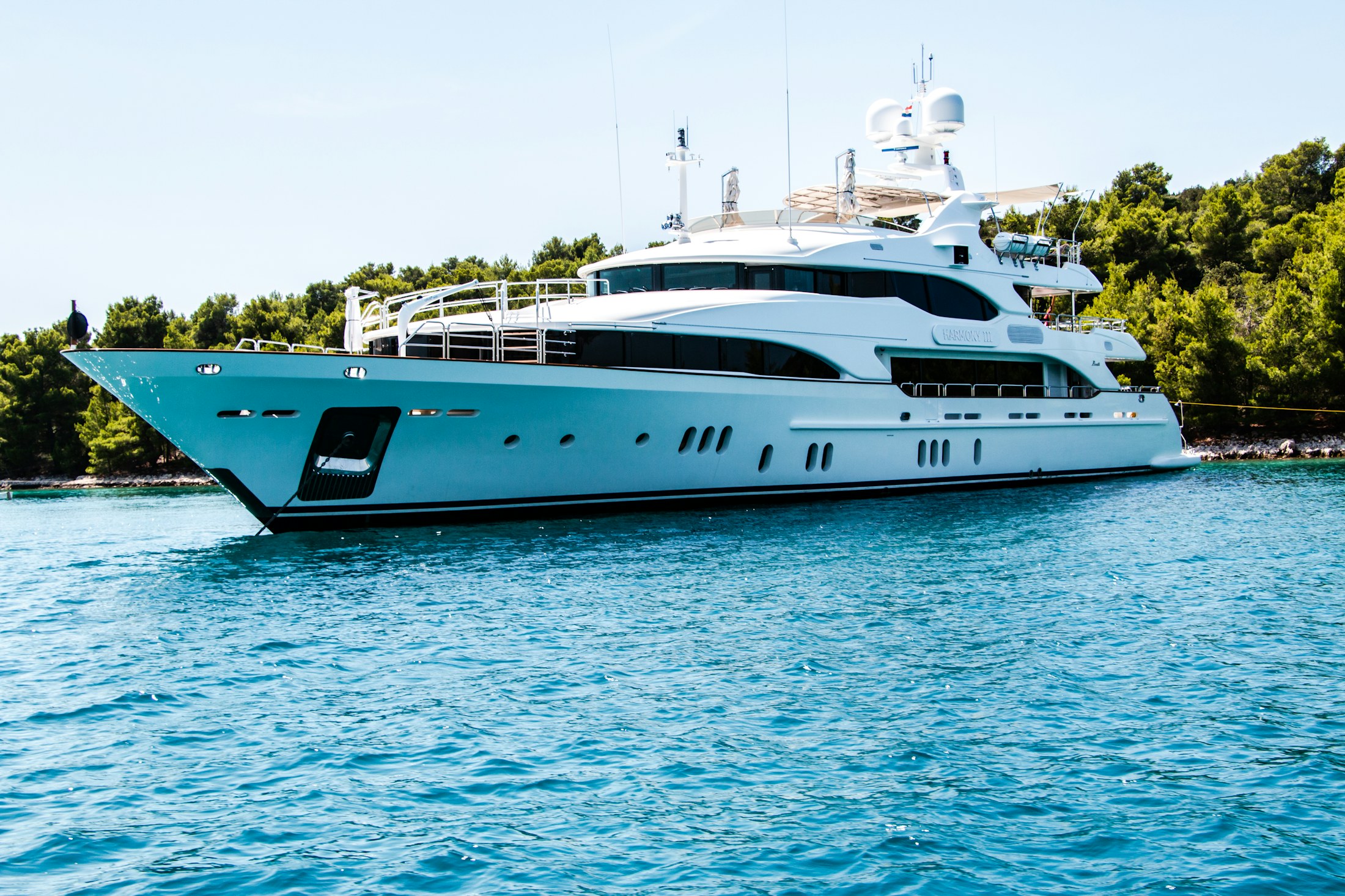 A large white motor yacht cruising through clear island water