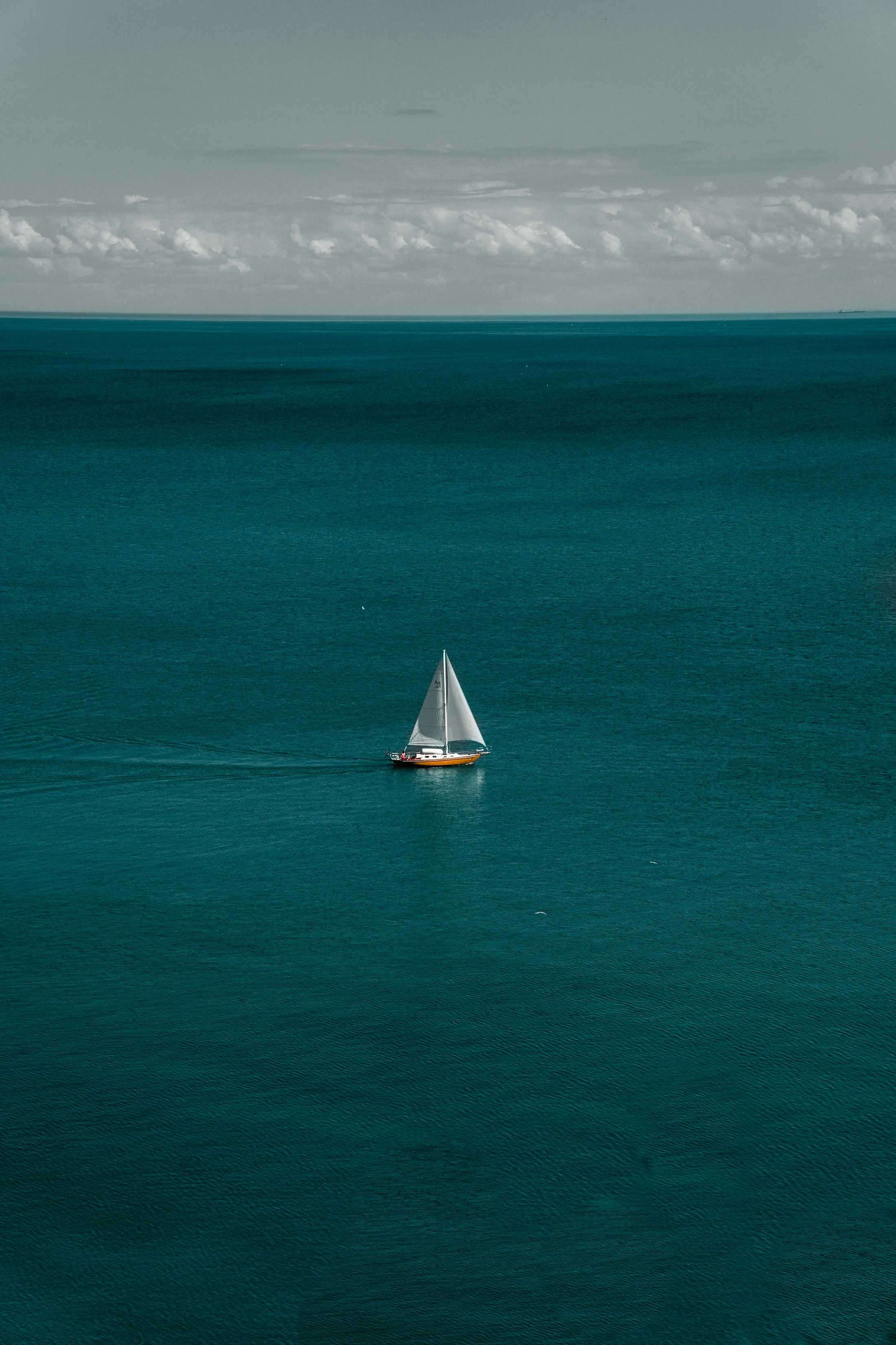 A lone sailboat crossing deep blue open water