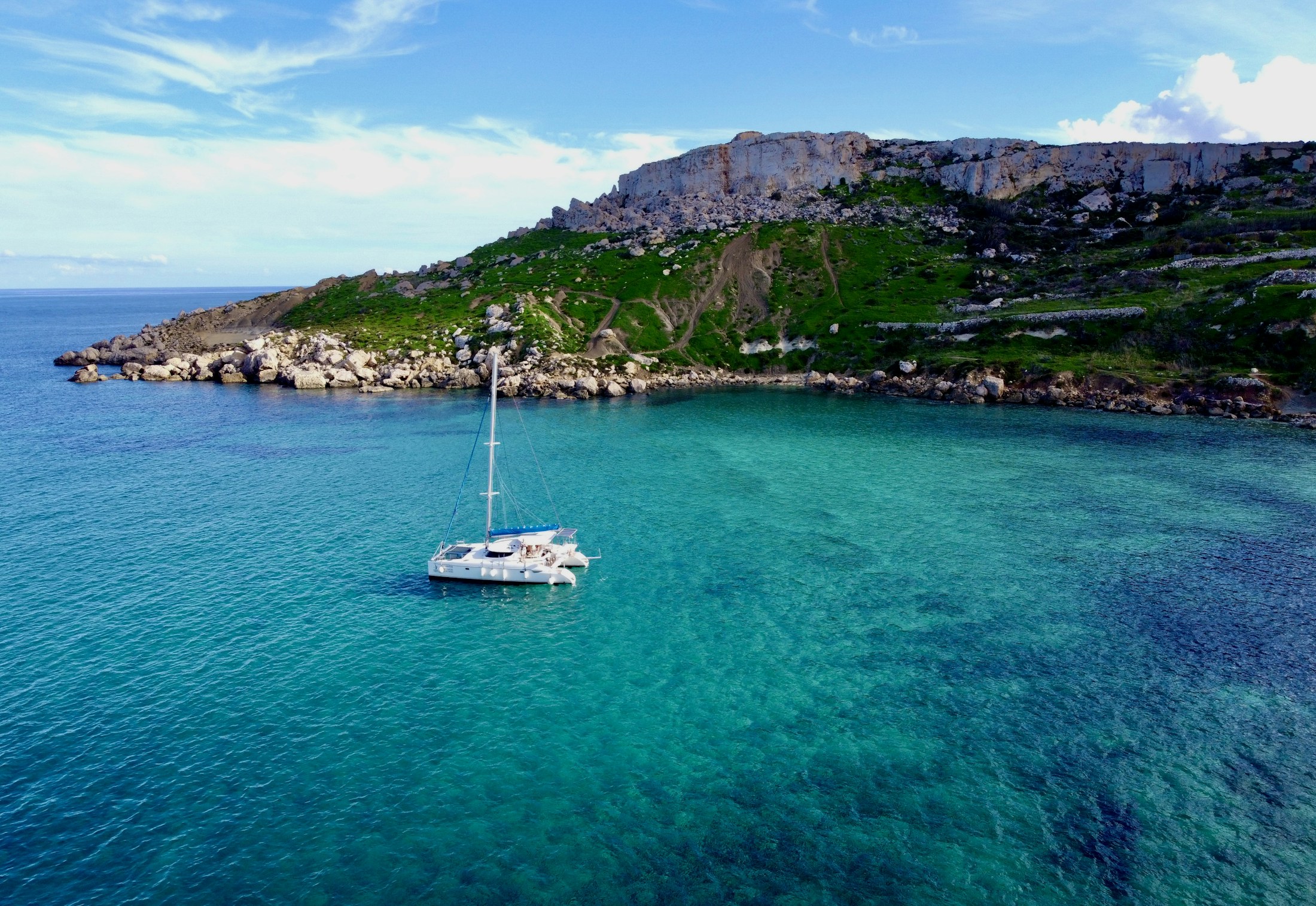 A sailing catamaran anchored in a clear island cove