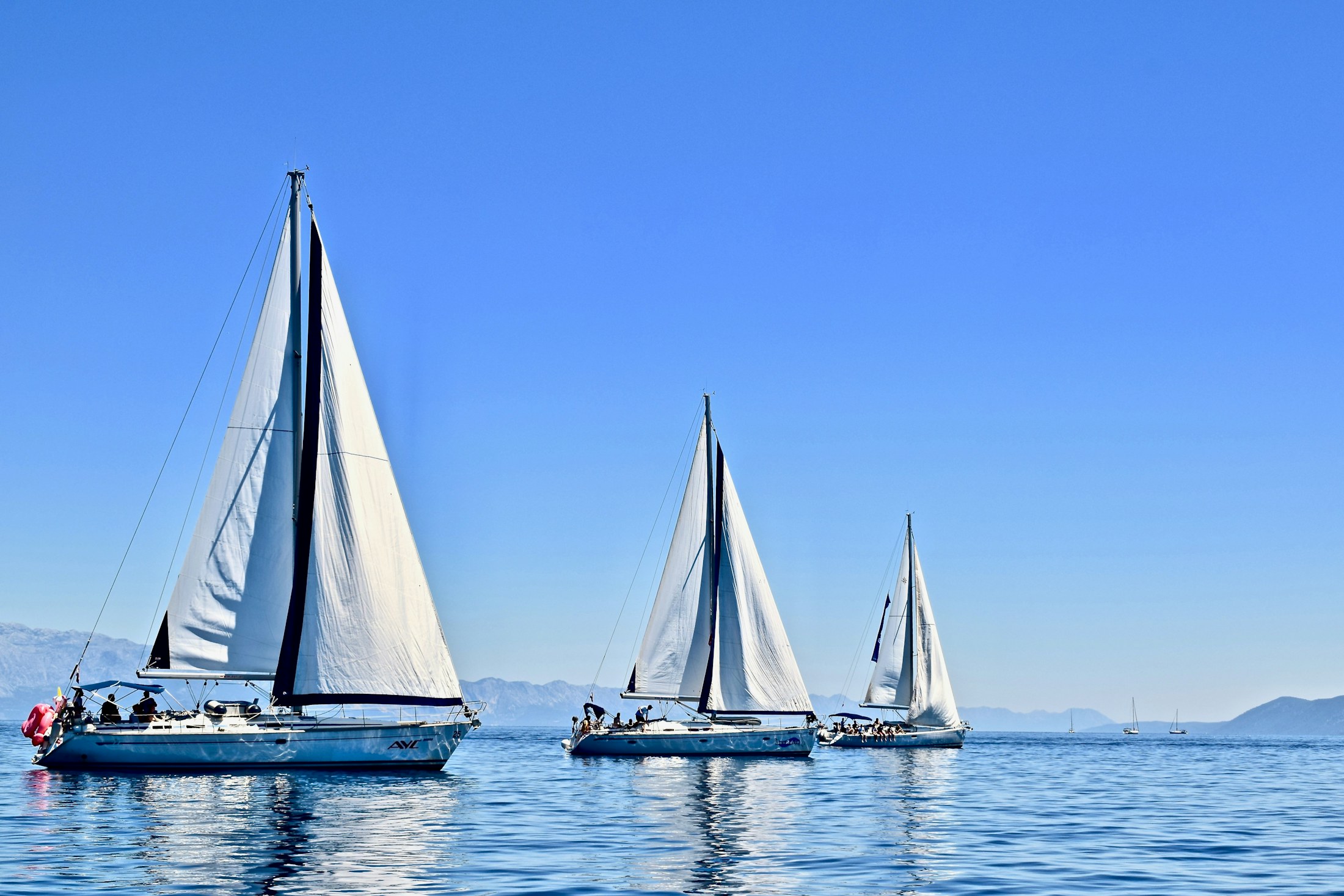 Three sailing yachts following separate lines across blue water